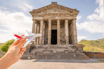 Tourist with a toy airplane on the background of a famous Garni Temple in Armenia. Concept of air flight transportation and travel