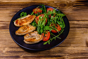 Roasted chicken breasts and salad with arugula and cherry tomatoes in a black plate