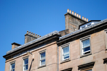 Fototapeta premium Detail of Facade & Roof Line of Old 19th Century Residential Tenement Building with Chimneys against Blue Sky