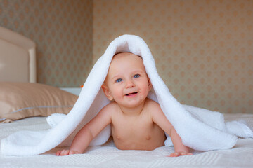 baby boy is covered with a white towel in the bedroom. A newborn baby is resting in bed after a bath or shower. Children's room. Textiles and bedding for children.