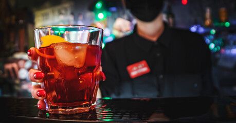 Closeup shot of bartender hand making negroni cocktail. Negroni classic cocktail and gin short drink with sweet vermouth, red bitter liqueur and dried orange garnish.