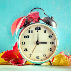 Daylight Saving Time concept, fall back in autumn, square image. A retro alarm clock with autumn...