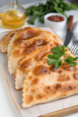 Board with delicious fried chebureki and parsley on white table, closeup