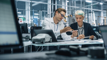 Two Young Automotive Engineers Working in Office at Car Factory. Industrial Designer and Colleague Discussing Different Applications of a Metal Pinion Gear in Personal Mobility Vehicles.