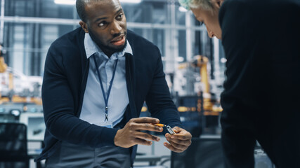 Two Young Automotive Engineers Working in Office at Car Factory. Industrial Designer and Colleague Discussing Different Applications of a Metal Pinion Gear in Personal Mobility Vehicles.