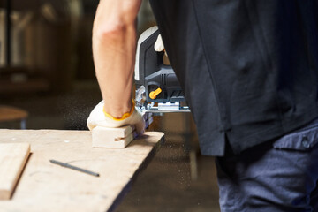 a man from the back saws off a piece of wood with a jigsaw - obrazy, fototapety, plakaty