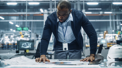 African American Engineer Looking at a Technical Blueprint at Work in an Office at Car Assembly...