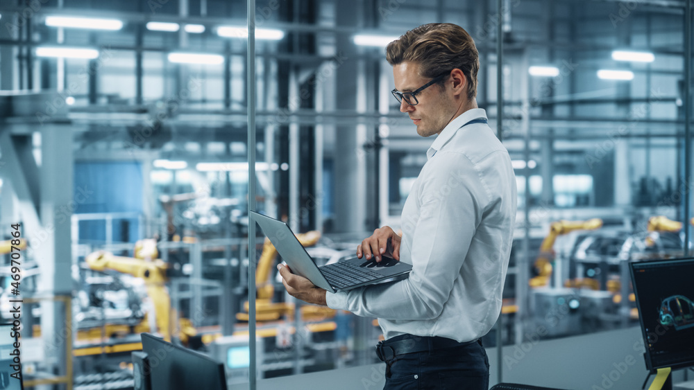 Poster handsome engineer in glasses and white shirt using laptop computer and looking out of the office at 