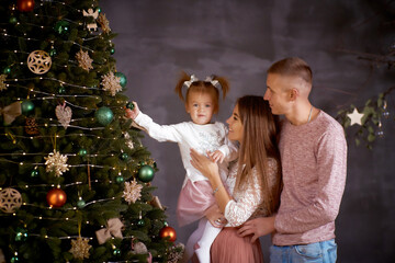 Young family with little baby girl in cozy home interior with festive Christmas tree. Good mood and...