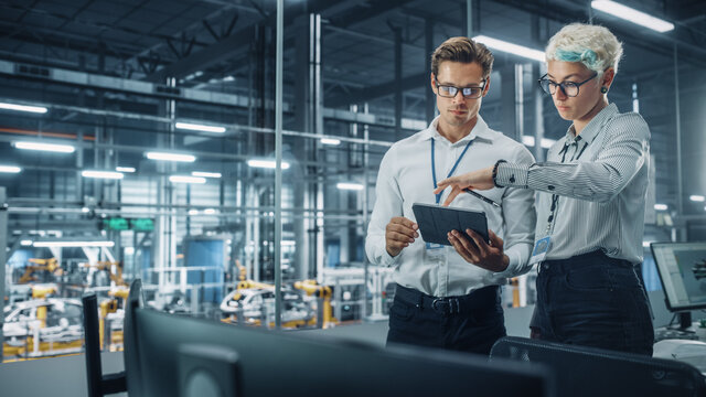 Male Engineer and Female Industrial Product Designer Discuss Work while Standing in Office at a Car Assembly Plant. Industrial Specialists Working on Vehicle Design in Technological Factory.