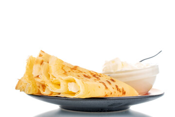 Several fragrant homemade pancakes on a ceramic plate and a saucer with sour cream, close-up, isolated on white.