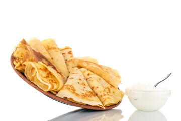 Several fragrant homemade pancakes on a ceramic plate and a saucer with sour cream, close-up, isolated on white.