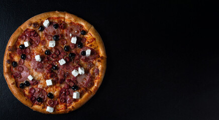 Spicy Sausage Pizza with food ingredients: cheese, sausage slice, pepperoni or salami, black olives and feta. On a black stone background. Fast food lunch, celebration. Top view. Banner. 
