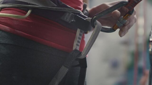Sport athletic woman secures the safety rope, carabiner hook. Attaches the belay to the carabiner. Climbing solo in indoor gym. Hobby in the city, healthy lifestyle. Slow motion