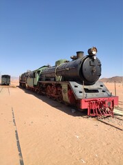 Fototapeta na wymiar Un ancien train transformé en musée, en Jordanie, près du désert Wadi Rum, transport industriel de passager ou de marchandises, sur des rails enfouis dans du sable, train à vapeur, ferroviaire 