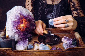 Glamorous woman in black dress cleansing crystals gemstones by smudging Palo Santo wood stick....