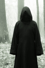 Death in a black hoodie mantle in forest mistery fog. Horror style fear spooky evil