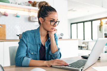 Pretty young woman working with laptop during morning coffee in the kitchen at home.