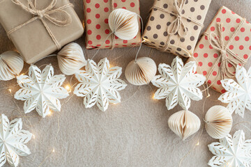 Fototapeta premium Beige paper gift boxes on a beige carpet lights Christmas garland and Christmas decorations made of paper. New Years celebration concept.