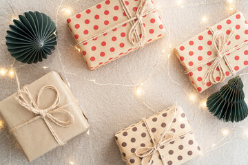 Beige paper gift boxes on a beige carpet lights Christmas garland and Christmas decorations made of paper. New Years celebration concept.