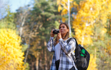 A female tourist walks in the forest with a camera and a backpack