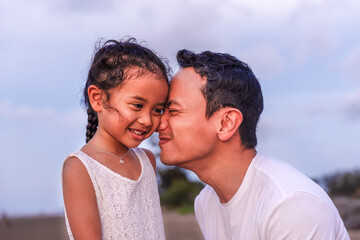 holidays, children and family concept -portrait of a little girl kissing her dad on cheek. Pretty girl giving a kiss to her father outdoor. Loving child embrace and kissing her father.