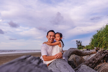 holidays, children and asian family concept -portrait of a little girl embrace her dad on the beach outdoor.