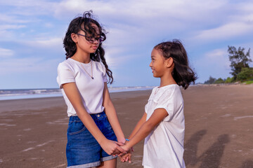 summer, childhood, leisure and people concept-two female asian siblings hold each other's hands