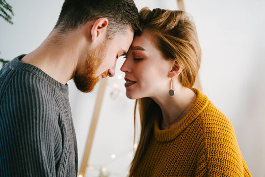 Romantic couple of lovers against the background of a Christmas tree made of natural wood. A girl in a yellow sweater and a guy in a gray one. Popular colors of 2021.