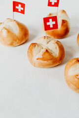 Swiss bread buns called in German 1. Augustweggen baked in Switzerland to celebrate Swiss National Day on August 1st. Swiss flag with white cross on red background. 