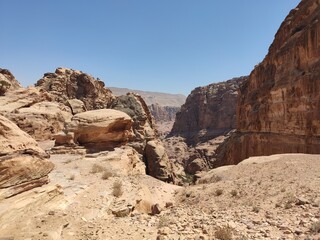 La cité nabatéenne Petra, située au sud de l'actuelle Jordanie, ancien chemin et marche sur des rochers rouges et oranges, forte chaleur et des cailloux, avec de la verdure et faille