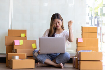 A young woman starting a small e-commerce business makes a cheerful gesture while chatting with customers on the Internet via laptop.