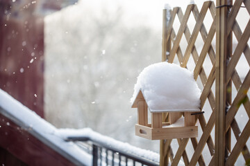 A simple handmade wooden bird feeder on a balcony on attic floor covered with thick snow at winter...