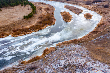 aerial top view of river bend with snowy frozen shore and bare trees in winter day