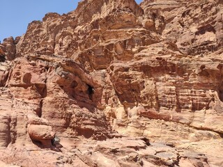 La cité nabatéenne Petra, située au sud de l'actuelle Jordanie, ancien chemin et marche sur des rochers rouges et oranges, forte chaleur et des cailloux, avec de la verdure et mur rocheux