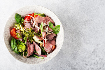 salad with roast beef and oyster mushrooms, herbs, cherry, basil and pesto sauce, gray background,...