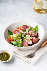 salad with roast beef and oyster mushrooms, herbs, cherry, basil and pesto sauce, gray background, glass of white wine