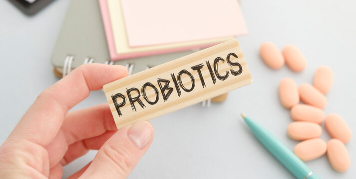 The word PROBIOTICS is written on a wooden block near the stethoscope, pills and syringe in hand on blue background. Medical concept