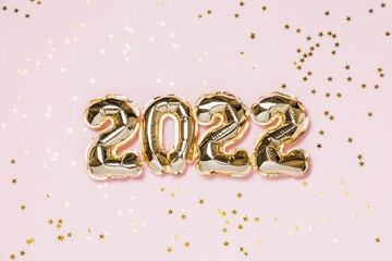 New year 2022 balloon celebration card. Gold foil balloon number 2022, party decoration, gold confetti on pink background. Flat lay, merry christmas, happy holidays concept.