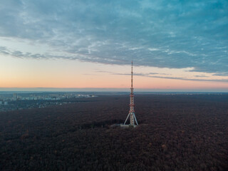 Aerial view after sunset, evening view on dark forest with telecommunication tower antenna and scenic cloudy sky. Kharkiv, Ukraine