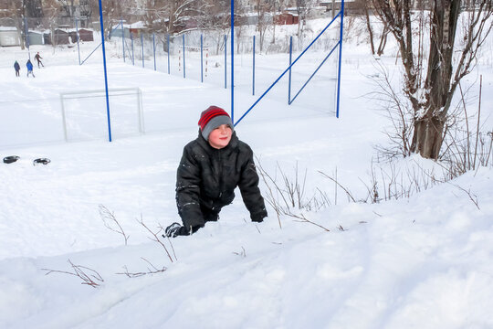 little boy playing in the snow, wearing a red hat, snowy, with a plasma plate for a slide,s kating rink  new year, christmas