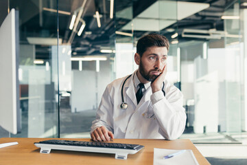 The doctor is a man working at the computer, tired and has severe toothache and headache, depressed working in the clinic