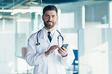 Male doctor in a white coat in a modern clinic reads information from a mobile phone corresponds...