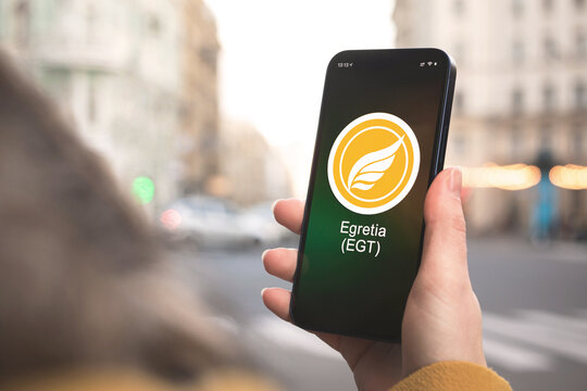 Egretia EGT cryptocurrency symbol, logo. Business and financial concept. Hand with smartphone, screen with crypto icon close-up