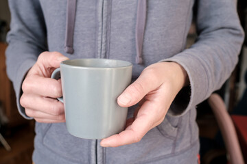 Female hands hold a mug of hot drink in the early morning in the apartment. 