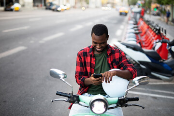 Handsome African man with scooter in the city. Young man using the phone.