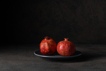 two ripe pomegranates lie on a gray plate on a dark background