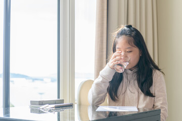 Little Girl drinking water sitting on a chair at home, Healthy