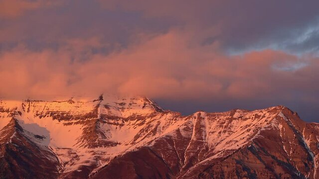Timpanogos Mountain snow capped glowing at sunset as clouds blow over the peaks in Utah.