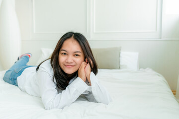 Portrait Cute Asian teen with long hair Wearing a white shirt and lazing around in bed happily in the bedroom.